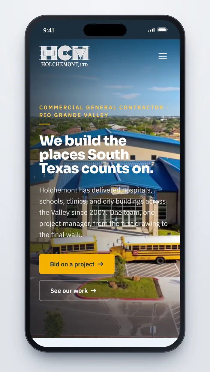 Holchemont's homepage on a phone: the eyebrow Commercial General Contractor, Rio Grande Valley, the headline We build the places South Texas counts on. over a photo of the finished blue-roofed building with yellow school buses out front, and stacked Bid on a project and See our work buttons.